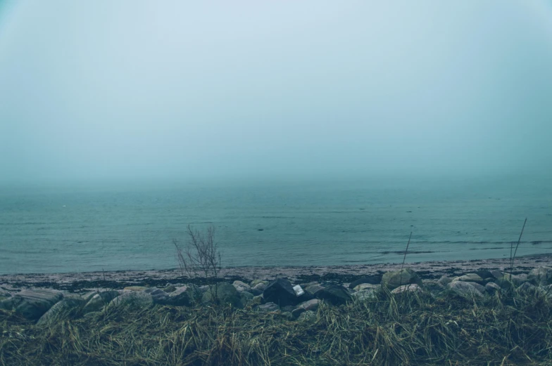 a rainbow over a body of water on a foggy day, a picture, inspired by Elsa Bleda, unsplash, romanticism, teal landscape, grey, depressing image, shoreline