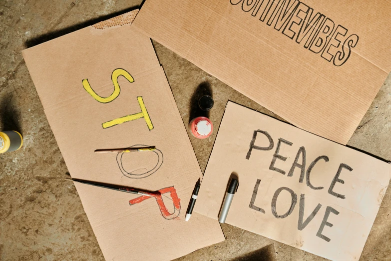 a couple of signs that are on the ground, by Julia Pishtar, trending on pexels, graffiti, cut out of cardboard, peace and love, art supplies, with some hand written letters