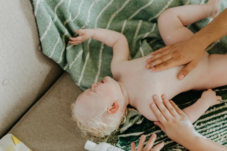 a baby laying on top of a couch next to a person, unsplash, oiled skin, manuka, air is being pushed around him, as well as the handyboy