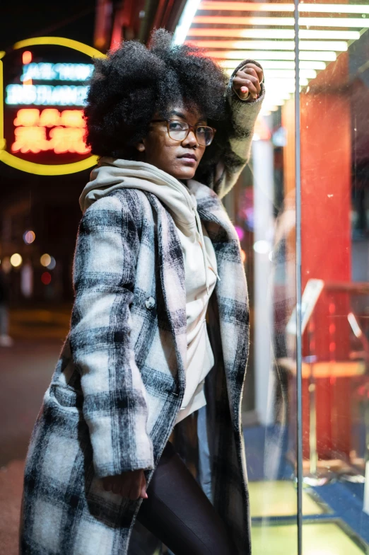 a woman standing in front of a store window, a portrait, by Dennis Flanders, trending on pexels, wearing a fur coat, nerdy black girl super hero, flannel, night life