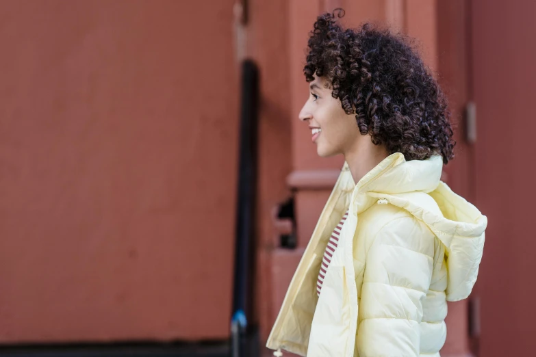 a woman with curly hair walking down the street, trending on pexels, happening, wearing a yellow hoodie, puffer jacket, pastel', shot on sony a 7