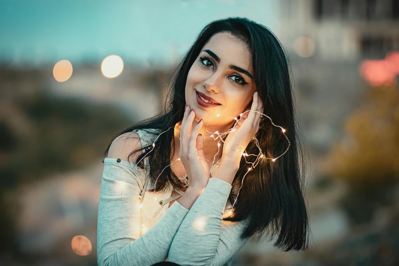 a woman holding a string of lights in front of her face, trending on pexels, beautiful iranian woman, lovingly looking at camera, instagram post, cute elegant pose