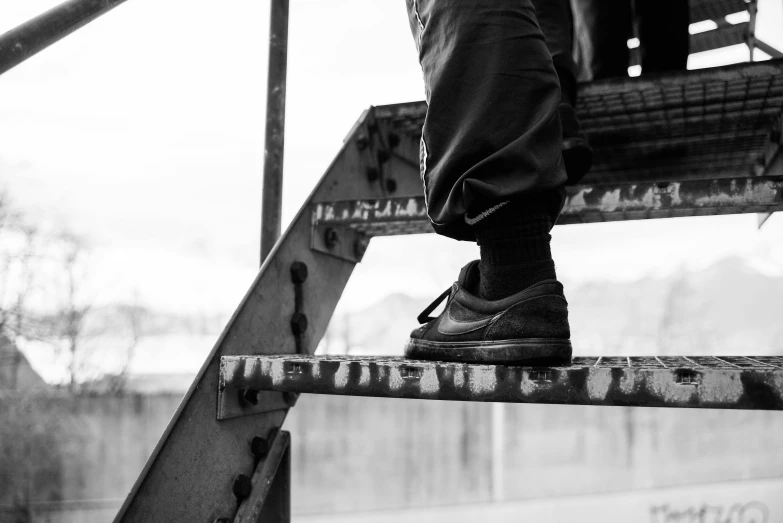 a person standing on a set of stairs, by Adam Marczyński, heavy-duty boots, close up portrait photo, black and grey, on a birdge