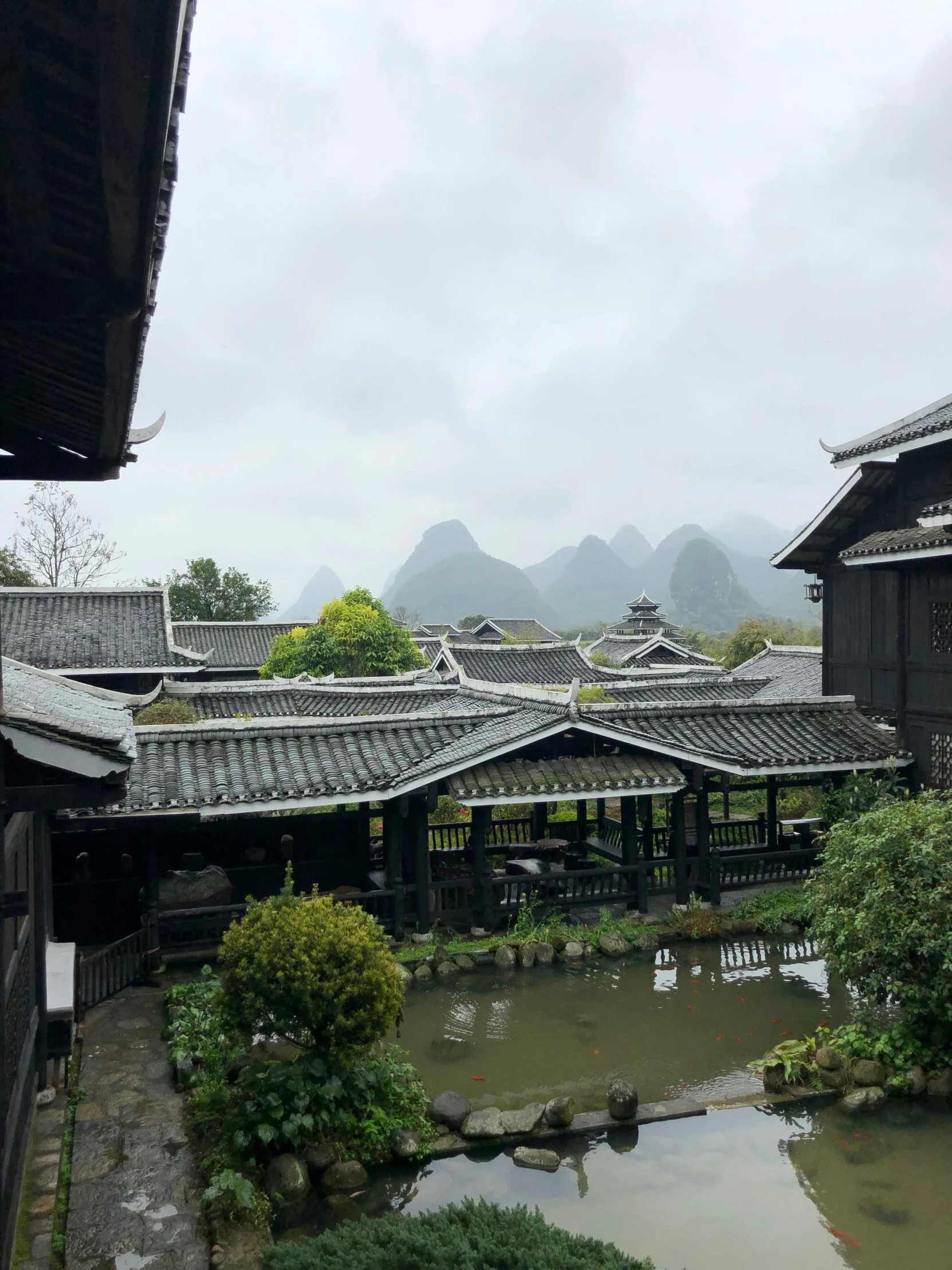 a number of buildings near a body of water, inspired by Li Keran, happening, beautiful mountains behind, rainy outside, thatched roofs, photo taken in 2018