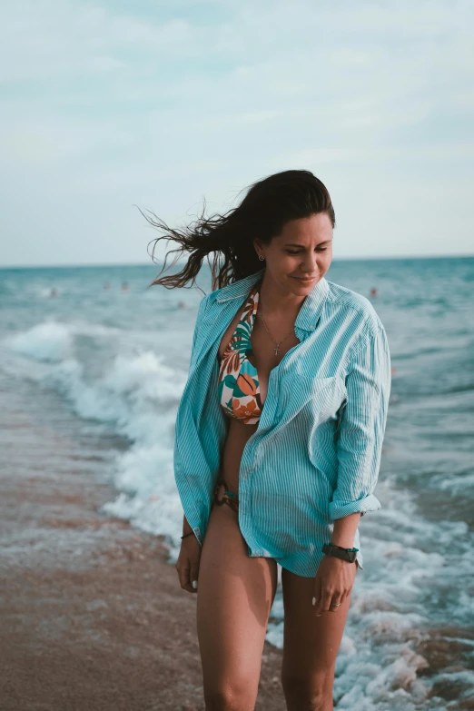 a woman standing on a beach next to the ocean, wearing a light blue shirt, deep in the ocean, wearing a shirt, profile image