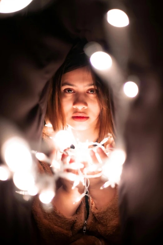 a woman holding a string of lights in her hands, pexels contest winner, light and space, serious composure, gif, multiple stories, teenage girl
