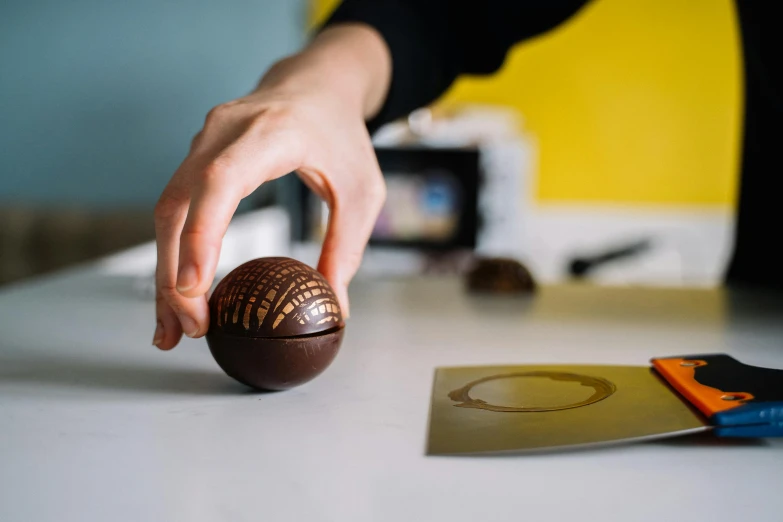 a person holding a chocolate ball on top of a table, pexels contest winner, engraved, product design shot, half turned around, slightly turned to the right