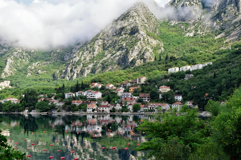 a group of boats floating on top of a lake, by Emma Andijewska, pexels contest winner, romanticism, boka, tiny village, mountainous setting, gray