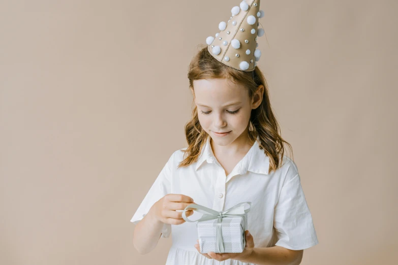 a little girl wearing a party hat and holding a present, pexels contest winner, wearing a white button up shirt, avatar image, abcdefghijklmnopqrstuvwxyz, wearing a paper crown