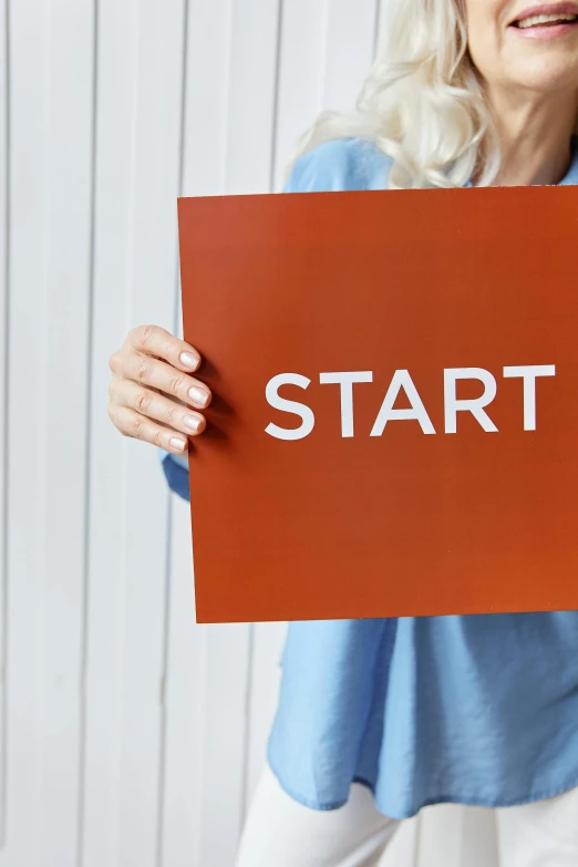 a woman holding a sign that says start, by karolis strautniekas, solid background, instagram post, istockphoto, high quality picture