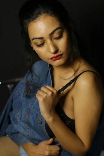 a beautiful young woman sitting on top of a bed, inspired by Moses Soyer, trending on pexels, denim jacket, provocative indian, close up half body shot, wearing black camisole outfit