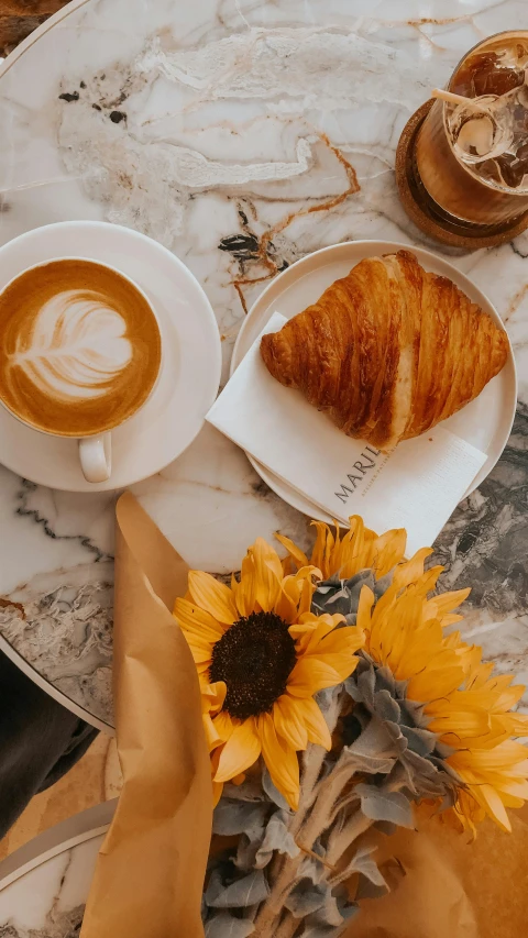 a person sitting at a table with a cup of coffee and croissants, by irakli nadar, pexels contest winner, colors : yellow sunflowers, marble and gold, thumbnail, square