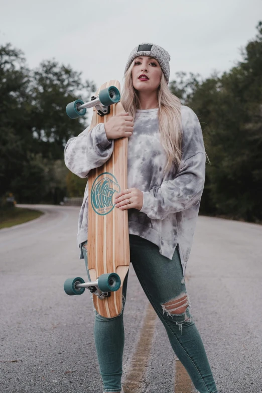 a woman standing on the side of a road holding a skateboard, a portrait, by McKendree Long, trending on unsplash, dressed in a gray, cottagecore hippie, split dye, cold as ice! 🧊