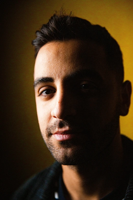 a man standing in front of a yellow wall, a character portrait, inspired by Nadim Karam, pexels contest winner, photorealism, in front of a black background, headshot profile picture, directional sunlight skewed shot, despacito