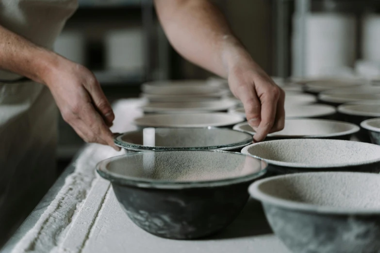 a person putting something in a bowl on a table, inspired by Lewis Henry Meakin, trending on unsplash, process art, in a row, cast iron material, made in tones of white and grey, pictured from the shoulders up