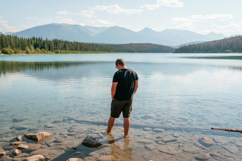 a man standing in the shallow waters of a lake, inspired by Michael James Smith, pexels contest winner, banff national park, looking at the ground, hot summer day, profile image