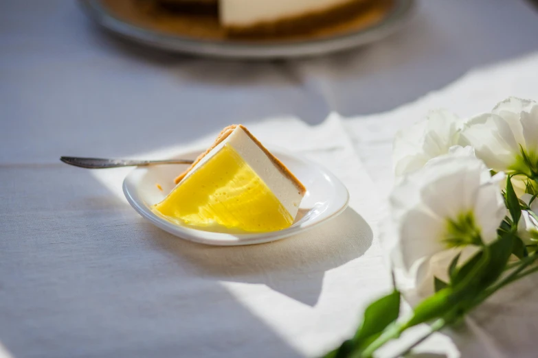 a piece of cheesecake sitting on top of a white plate, a still life, by Sylvia Wishart, unsplash, art nouveau, bright sunny day, glossy yellow, glass tableware, deckle edge