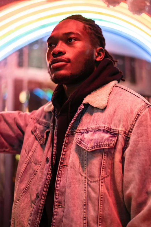 a man standing in front of a neon sign, trending on pexels, brown skin, wearing jeans and a black hoodie, profile image, smirking