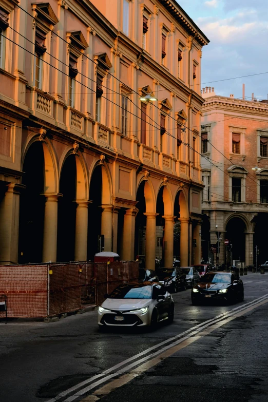 a group of cars driving down a street next to tall buildings, renaissance, italian renaissance architecture, bathed in golden light, neoclassical police station, black and terracotta