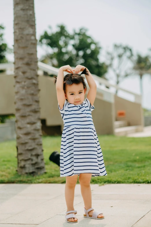 a little girl standing on top of a sidewalk, small heart - shaped face, with arms up, stripes, blue-white dress