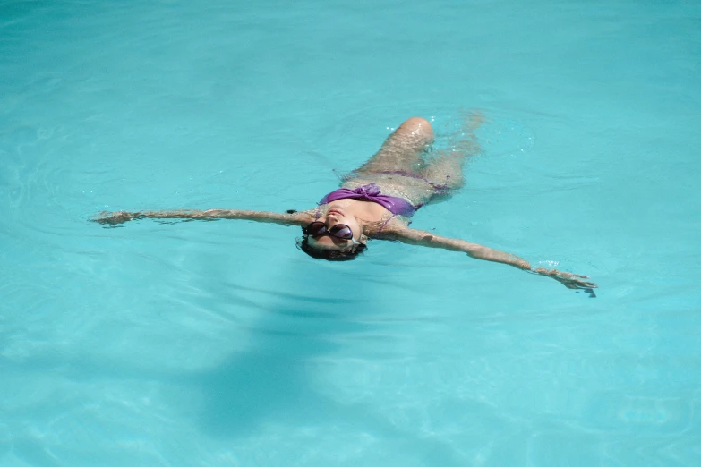 a woman in a purple bikini swims in a pool, by Jessie Algie, pexels contest winner, arms stretched out, no words 4 k, aquatic devices, head straight down