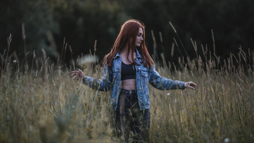 a woman standing in a field of tall grass, inspired by Elsa Bleda, pexels contest winner, wearing a jeans jackets, long straight red hair, battle pose, various posed