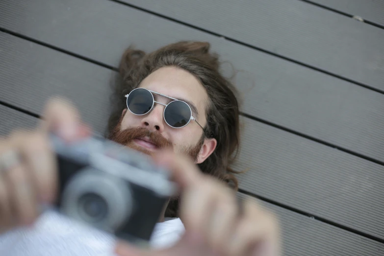 a man taking a picture of himself with a camera, a picture, pexels contest winner, photorealism, lying down, beard, shades, top down perspecrive