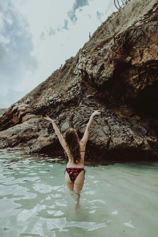 a woman in a bikini standing in a body of water, pexels contest winner, girl dancing on cliff, australian beach, standing in a grotto, pose(arms up + happy)