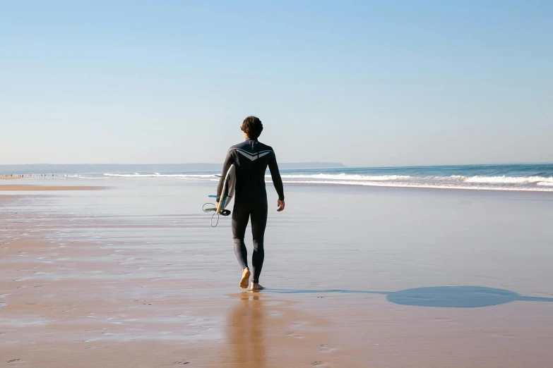 a person walking on a beach with a surfboard, pexels contest winner, man in dark blue full body suit, omaha beach, profile image, thumbnail