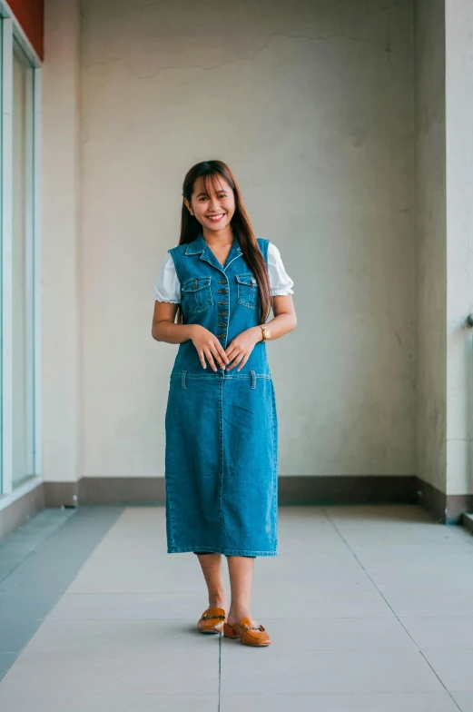 a woman in a blue dress standing in front of a window, inspired by Ruth Jên, unsplash, wearing overalls, wearing school uniform, portrait of modern darna, long dress