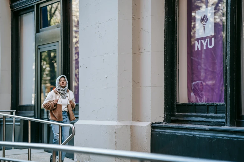 a woman walking down a sidewalk next to a building, a photo, hurufiyya, in the middle of new york, official store photo, portrait featured on unsplash, an arab standing watching over