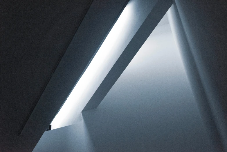 a light shines through a window in a dark room, inspired by Zaha Hadid, light and space, slanted ceiling, white light, soft blue lighting, 5000k white product lighting