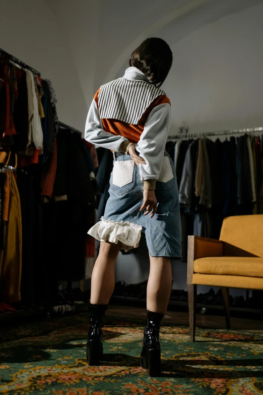 a woman standing in front of a rack of clothes, by Adam Saks, happening, back view. nuri iyem, off-white, wearing victorian rags, cropped shirt with jacket