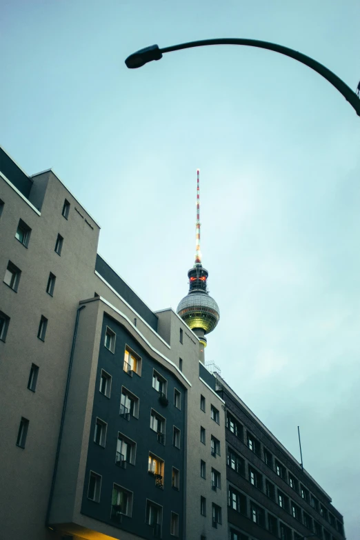 a tall building with a television tower in the background, a photo, trending on unsplash, berlin secession, topknot, view from the streets, lit from below, long neck