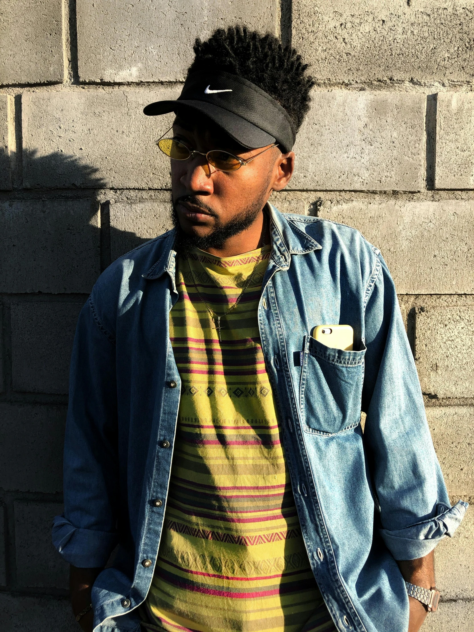 a man standing in front of a brick wall, an album cover, trending on unsplash, black arts movement, wearing yellow croptop, wearing stripe shirt, faded out colors, headshot profile picture