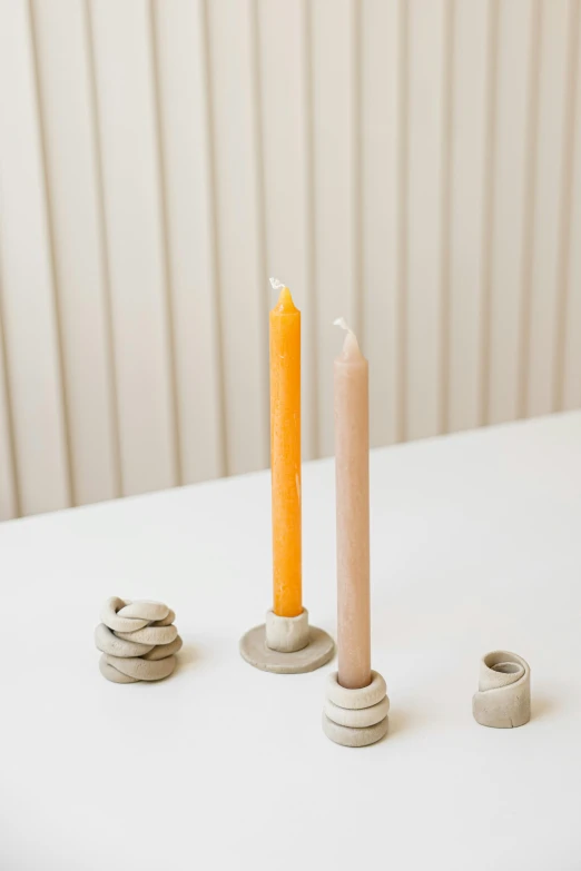 a couple of candles sitting on top of a table, an abstract sculpture, inspired by Giorgio Morandi, minimalism, spiral, midsommar color theme, clay material, various sizes