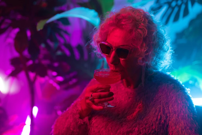 a woman sitting at a table with a drink in her hand, inspired by Elsa Bleda, pexels, maximalism, cinematic neon uplighting, an old lady, party in jungles, still from a live action movie