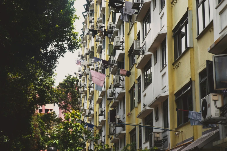 a group of people walking down a street next to tall buildings, inspired by Elsa Bleda, unsplash, renaissance, laundry hanging, yellowed with age, set on singaporean aesthetic, soviet apartment building