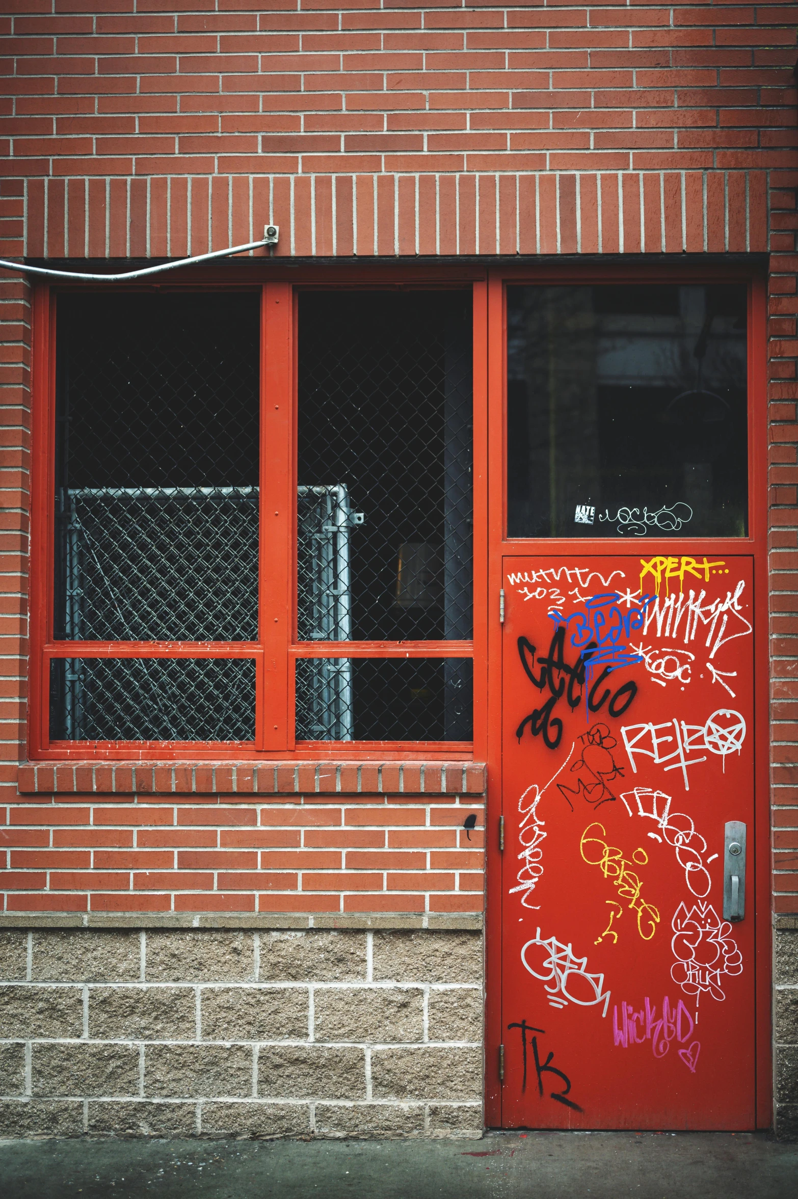 a red door with graffiti on it in front of a brick building, inspired by Elsa Bleda, graffiti, ignant, low quality photo, private school, windows and walls :5