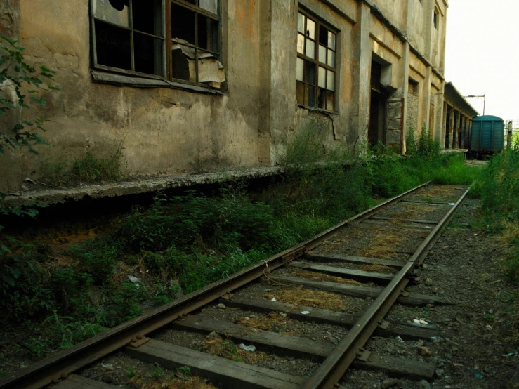 a train track that is next to a building, by Lucia Peka, abandoned photograph, cinematic film still, ((rust)), green alleys