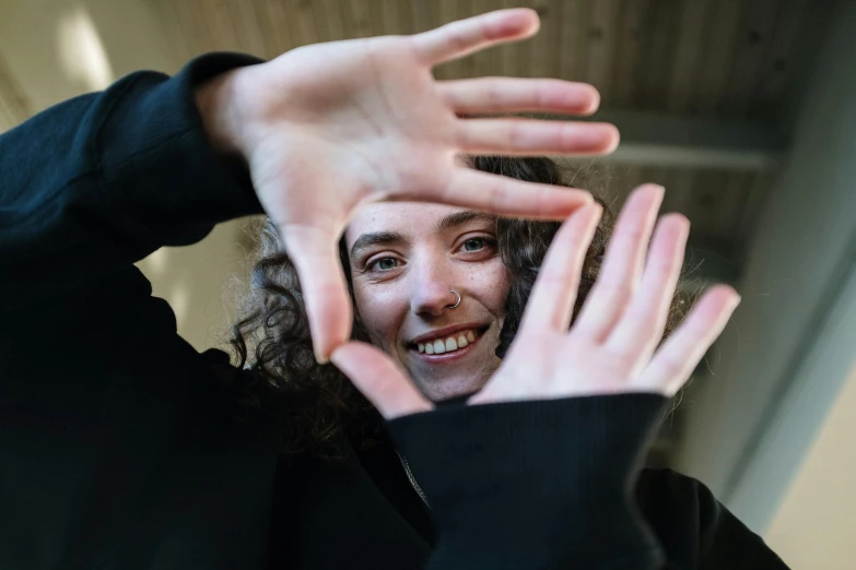 a person making a heart with their hands, by Matthias Stom, pexels contest winner, visual art, her face framed with curls, smiling at camera, wave a hand at the camera, timothee chalamet