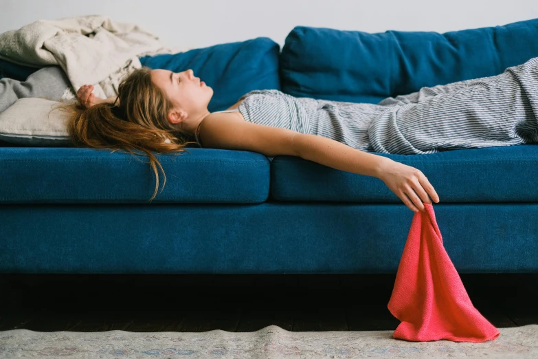 a woman laying on top of a blue couch, by Julia Pishtar, pexels contest winner, happening, flowing mucus, heat wave, sydney sweeney, furniture overturned