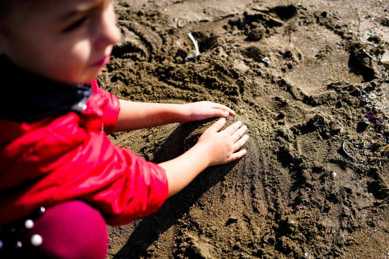 a small child playing in the sand at the beach, by Daniel Lieske, pexels, land art, at an archaeological dig site, promo image, hand, schools