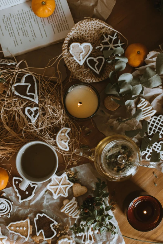 an open book sitting on top of a table next to a cup of coffee, a still life, trending on pexels, folk art, gingerbread people, the candle is on a wooden table, romantic greenery, scattered props