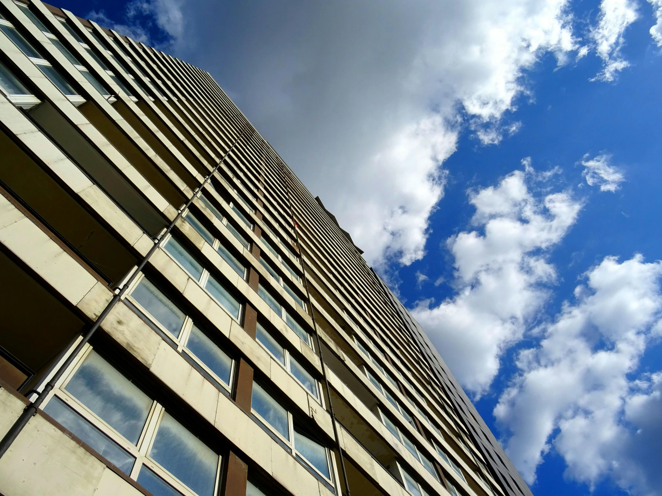 a tall building with lots of windows under a cloudy blue sky, inspired by Richard Wilson, unsplash, brutalism, ten flats, 2 0 0 0's photo