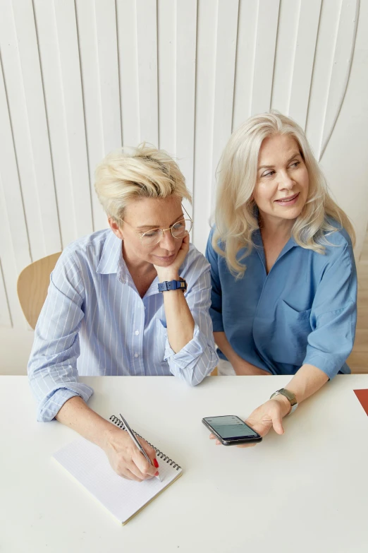 two women sitting at a table looking at a cell phone, trending on pexels, renaissance, white haired lady, professional photo, sitting on a desk, avatar image