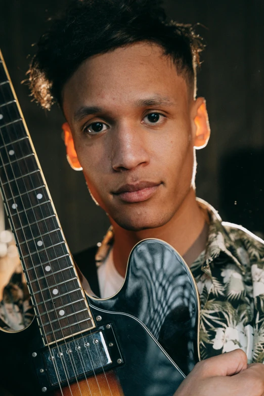 a close up of a person holding a guitar, an album cover, inspired by David Brewster, pexels contest winner, photorealism, mixed race, thin young male, half onesided smile, nonbinary model