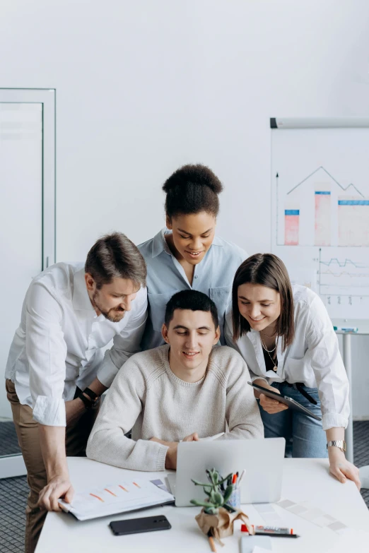 a group of people standing around a table with a laptop, on top of it