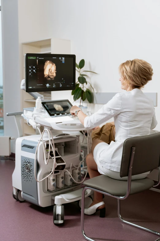 a woman sitting in a chair in front of a computer, digital medical equipment, femme fetal, intricate features, grey
