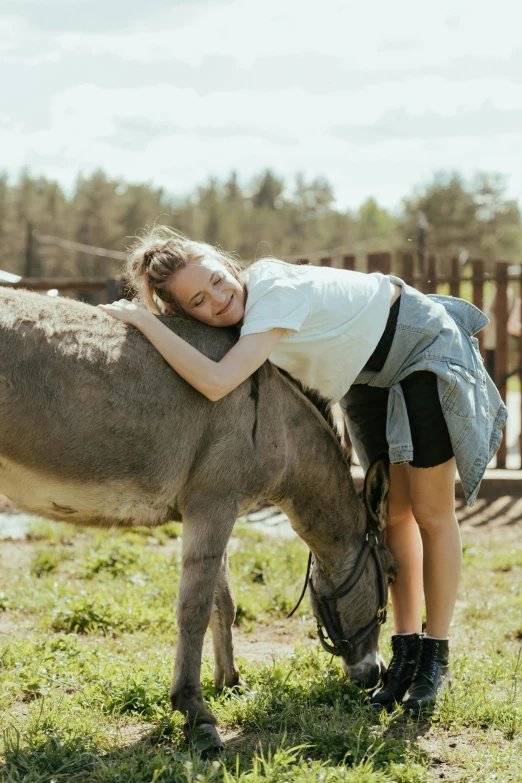 a woman standing next to a donkey on a lush green field, by Julia Pishtar, petting zoo, russian girlfriend, hugging her knees, scandinavian